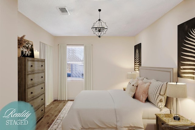 bedroom featuring a notable chandelier, visible vents, a textured ceiling, and wood finished floors