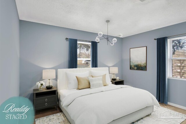 bedroom featuring a notable chandelier, wood finished floors, baseboards, and a textured ceiling