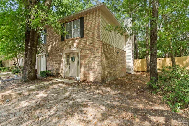 view of front of home with fence, a chimney, and brick siding