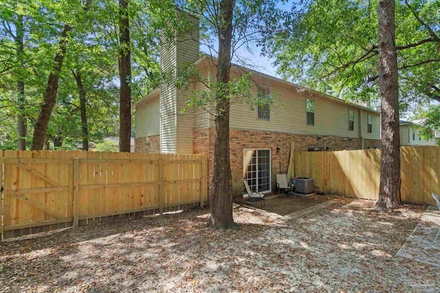 back of property with brick siding, fence, central air condition unit, and a chimney