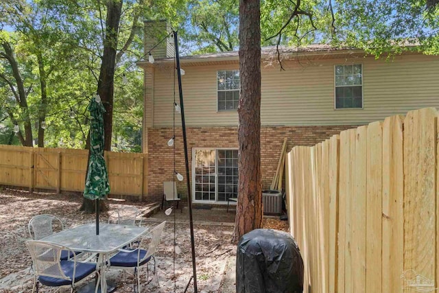back of property featuring fence, outdoor dining area, a chimney, brick siding, and central AC unit