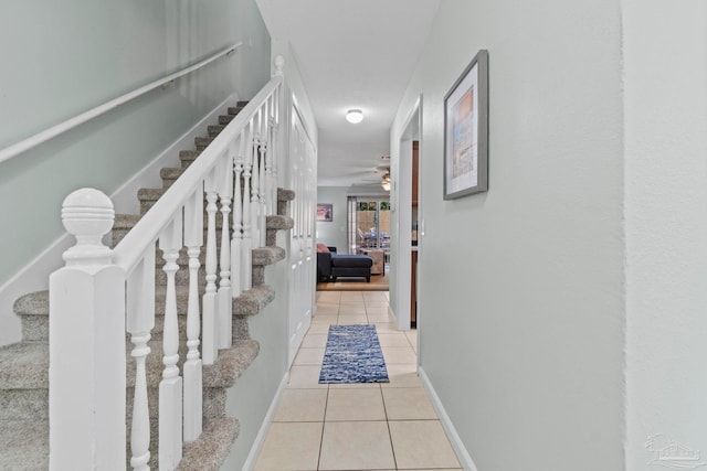 hallway with baseboards, light tile patterned flooring, and stairway