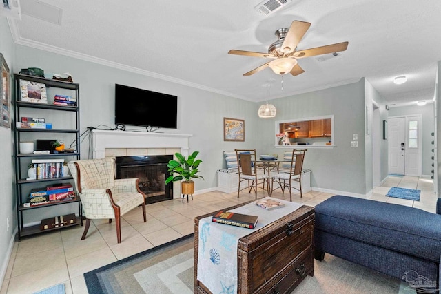 tiled living room with ceiling fan, visible vents, a tile fireplace, baseboards, and ornamental molding