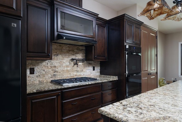 4513 River Ranch Rd, Milton, FL 32583 - kitchen featuring black appliances, tasteful backsplash, under cabinet range hood, dark brown cabinetry, and light stone countertops