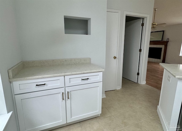 kitchen with light stone countertops, white cabinetry, ceiling fan, and light tile patterned flooring