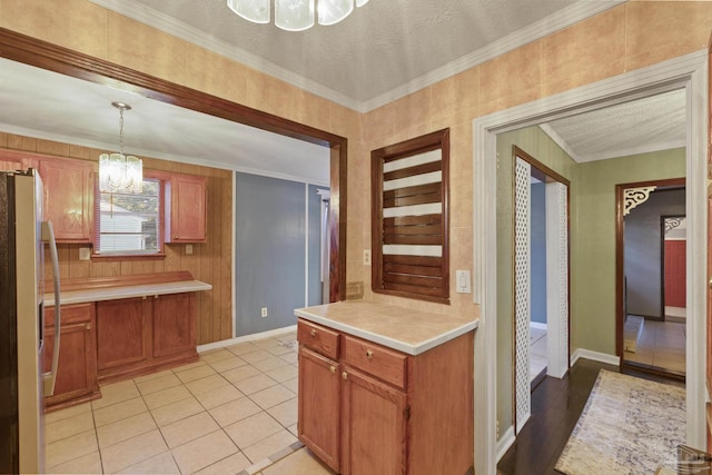 kitchen featuring light tile patterned floors, stainless steel fridge, a notable chandelier, ornamental molding, and decorative light fixtures