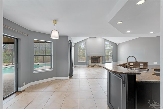 kitchen featuring pendant lighting, a stone fireplace, sink, dark stone countertops, and light tile patterned flooring