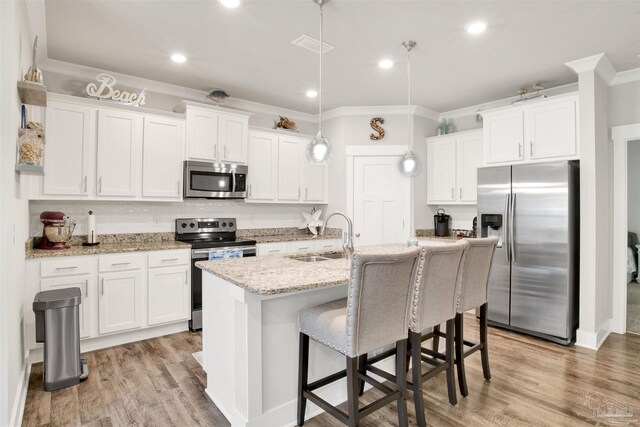 kitchen featuring decorative light fixtures, light hardwood / wood-style flooring, appliances with stainless steel finishes, sink, and white cabinets