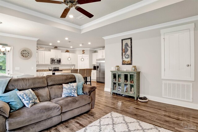 living room featuring ceiling fan with notable chandelier, a raised ceiling, ornamental molding, and light hardwood / wood-style flooring