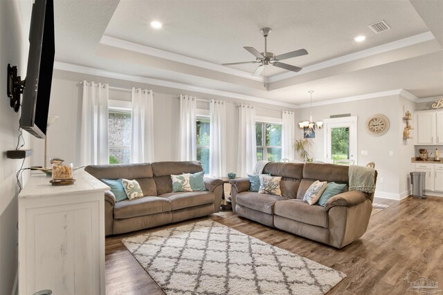 living room with ceiling fan with notable chandelier, a raised ceiling, ornamental molding, and light hardwood / wood-style floors