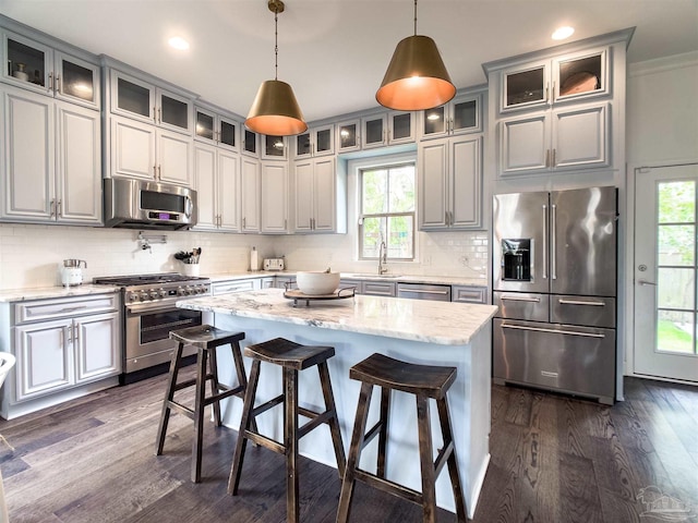 kitchen with hanging light fixtures, dark hardwood / wood-style floors, a center island, high end appliances, and light stone counters