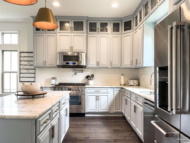 kitchen featuring decorative light fixtures, tasteful backsplash, high end appliances, light stone counters, and dark wood-type flooring