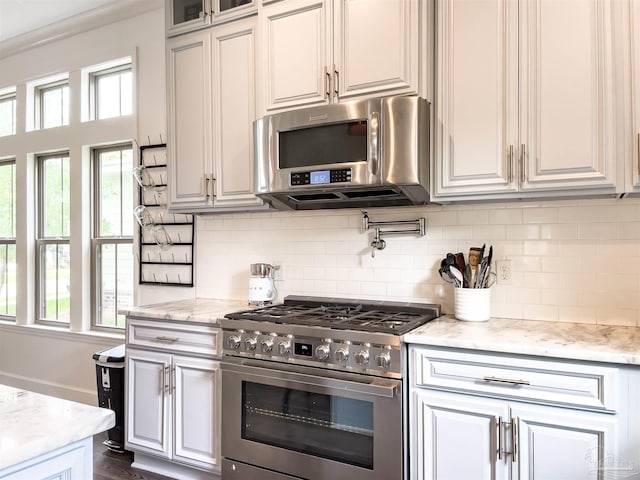 kitchen with stainless steel appliances, white cabinetry, light stone counters, and decorative backsplash