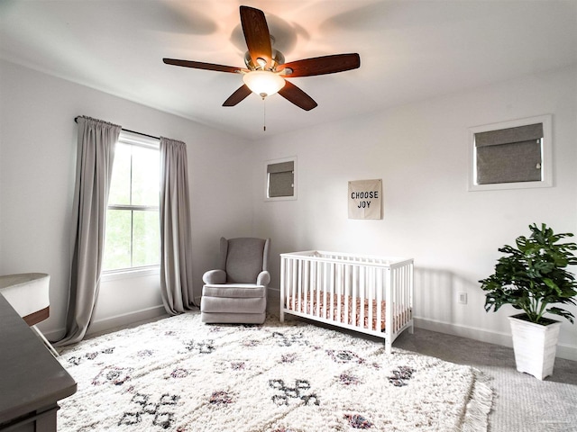 carpeted bedroom featuring ceiling fan and a crib