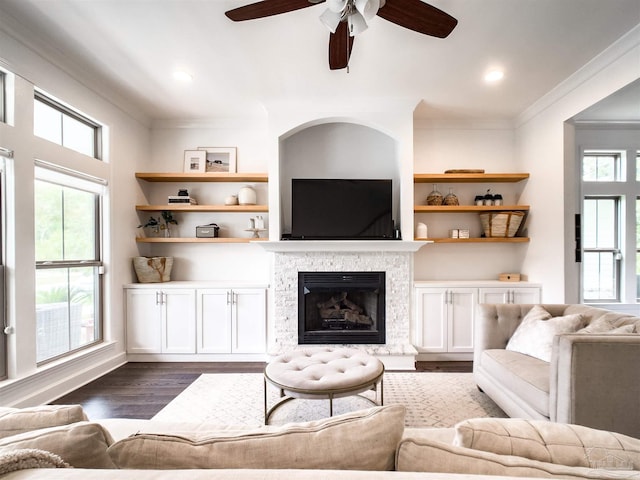 living room featuring ornamental molding, a healthy amount of sunlight, dark hardwood / wood-style floors, and a stone fireplace