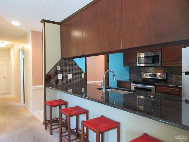 kitchen with stainless steel appliances, dark stone countertops, kitchen peninsula, and sink