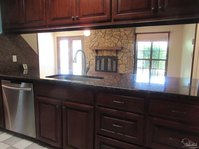 kitchen with stainless steel dishwasher, sink, a stone fireplace, and tasteful backsplash