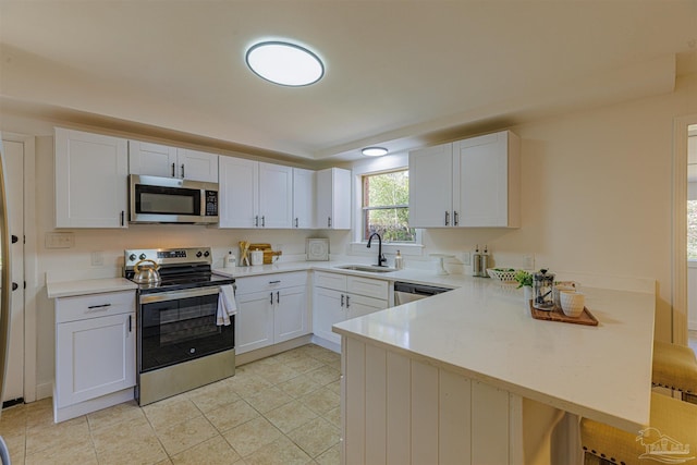 kitchen with a peninsula, a sink, light countertops, appliances with stainless steel finishes, and white cabinetry