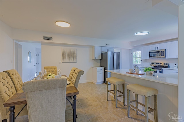 kitchen featuring visible vents, stainless steel appliances, light countertops, white cabinetry, and a kitchen breakfast bar