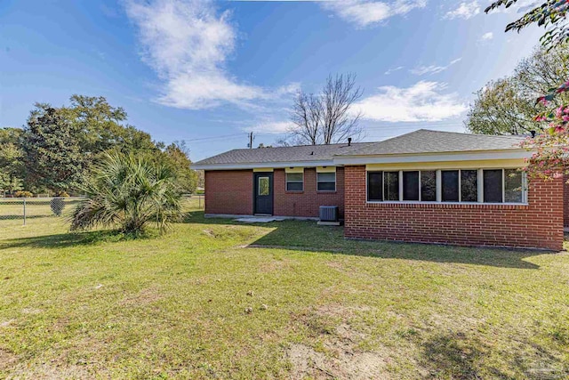 rear view of house with a yard, central air condition unit, brick siding, and fence