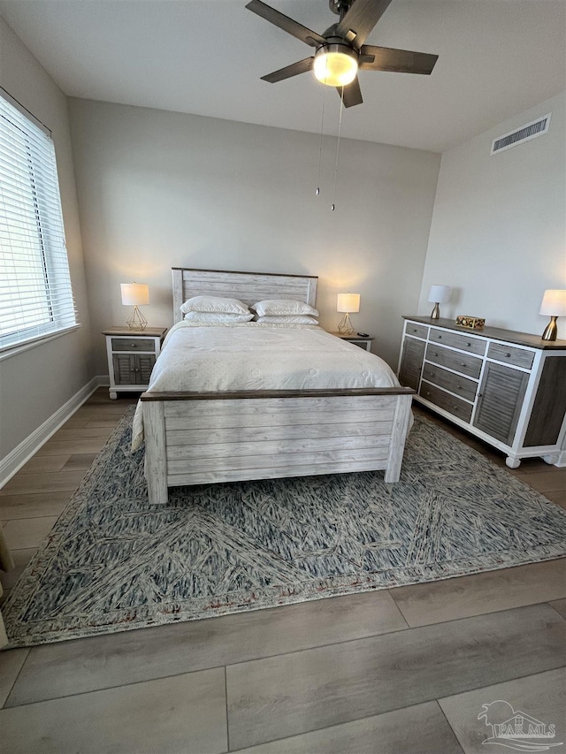 bedroom with a ceiling fan, wood finished floors, baseboards, and visible vents