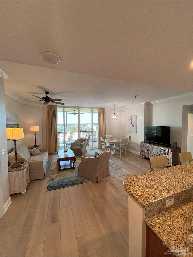 living area with baseboards, ceiling fan, light wood-type flooring, and crown molding