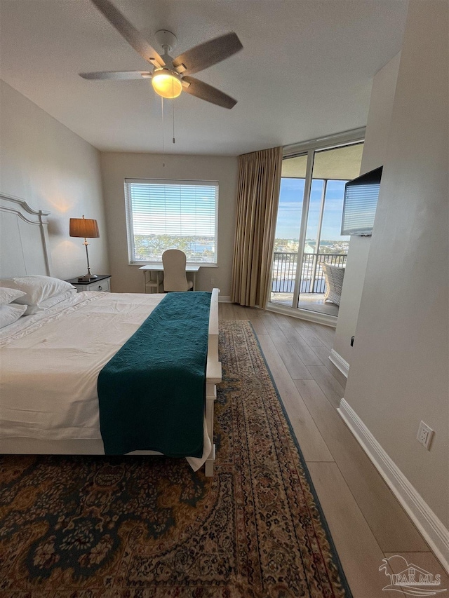 bedroom featuring expansive windows, wood finished floors, access to outside, baseboards, and ceiling fan