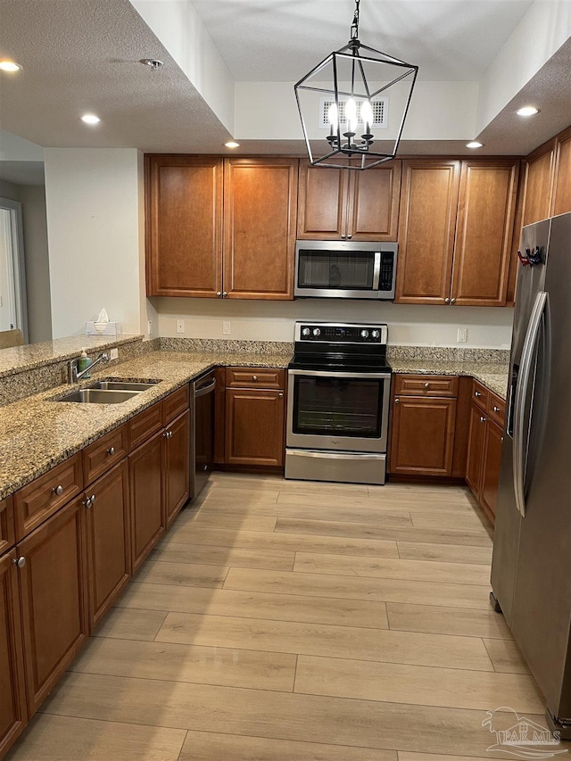 kitchen with a sink, light stone countertops, appliances with stainless steel finishes, light wood-style floors, and recessed lighting
