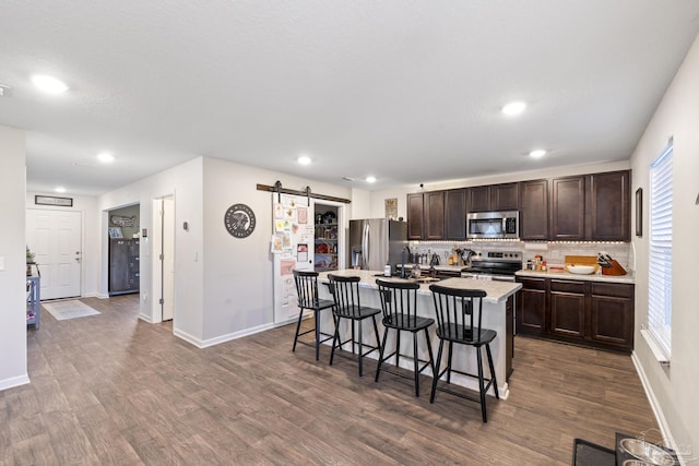 4678 Perception Cir, Milton, FL 32570 - kitchen featuring appliances with stainless steel finishes, a barn door, dark brown cabinetry, a kitchen bar, and dark wood finished floors
