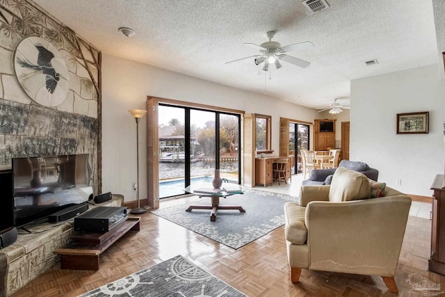 living area featuring visible vents, ceiling fan, a textured ceiling, and baseboards