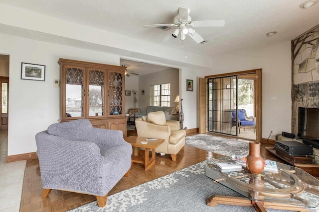 living area with ceiling fan, a textured ceiling, and baseboards