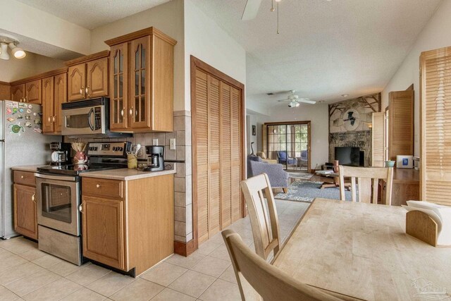 kitchen featuring ceiling fan, light tile patterned floors, open floor plan, appliances with stainless steel finishes, and glass insert cabinets