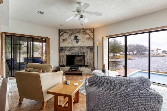 living area featuring a textured ceiling, ceiling fan, a water view, and visible vents