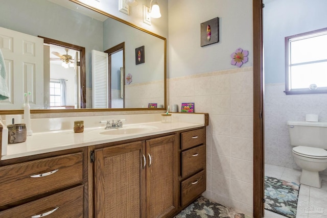 bathroom with wainscoting, toilet, tile patterned flooring, vanity, and tile walls