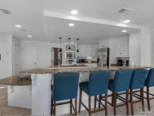 kitchen featuring stone counters, white cabinets, a kitchen bar, hanging light fixtures, and stainless steel appliances