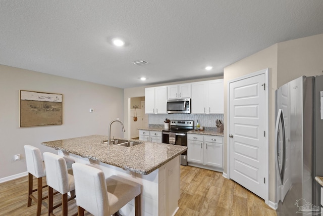 5711 Guinevere Ln, Milton, FL 32583 - kitchen with light wood-type flooring, an island with sink, white cabinetry, stainless steel appliances, and a sink