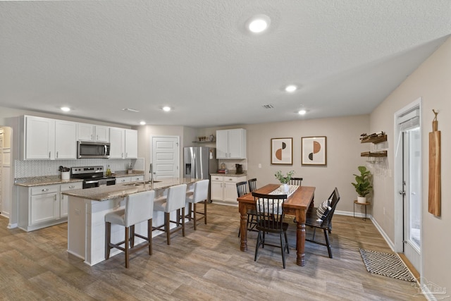 5711 Guinevere Ln, Milton, FL 32583 - kitchen with white cabinetry, appliances with stainless steel finishes, a kitchen breakfast bar, and wood finished floors
