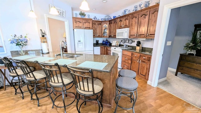 kitchen with pendant lighting, white appliances, sink, light hardwood / wood-style floors, and a breakfast bar