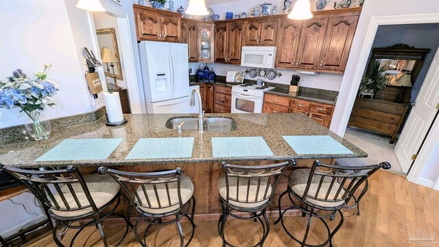 kitchen featuring a breakfast bar, light hardwood / wood-style flooring, white appliances, kitchen peninsula, and sink