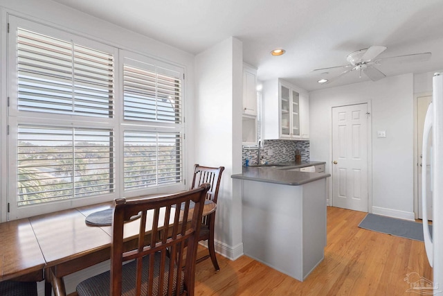 kitchen with decorative backsplash, a sink, ceiling fan, white cabinets, and glass insert cabinets