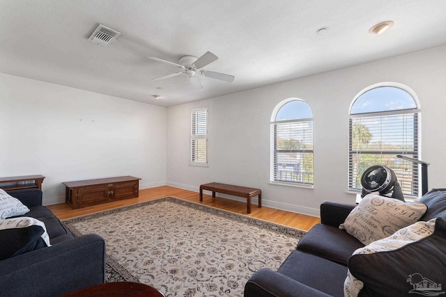 living area with a ceiling fan, wood finished floors, baseboards, and visible vents