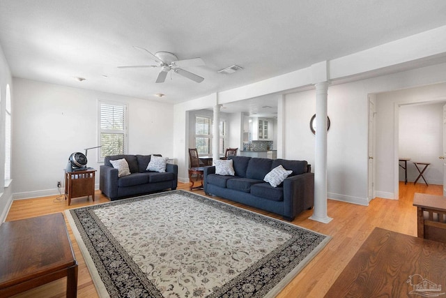 living room with decorative columns, visible vents, light wood-style flooring, and a ceiling fan