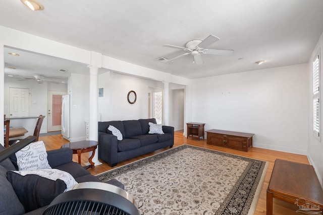 living room with light wood-style flooring, visible vents, ornate columns, baseboards, and ceiling fan