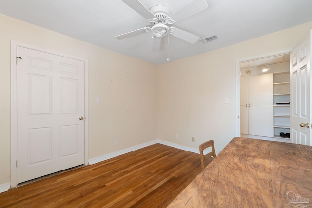 unfurnished room featuring baseboards, visible vents, wood finished floors, and a ceiling fan