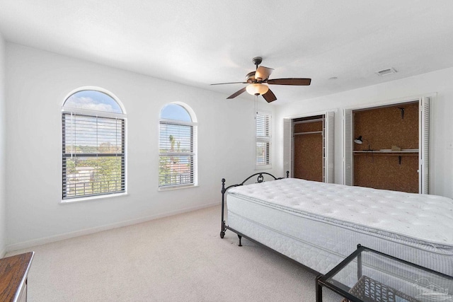 bedroom with carpet floors, multiple closets, baseboards, visible vents, and ceiling fan
