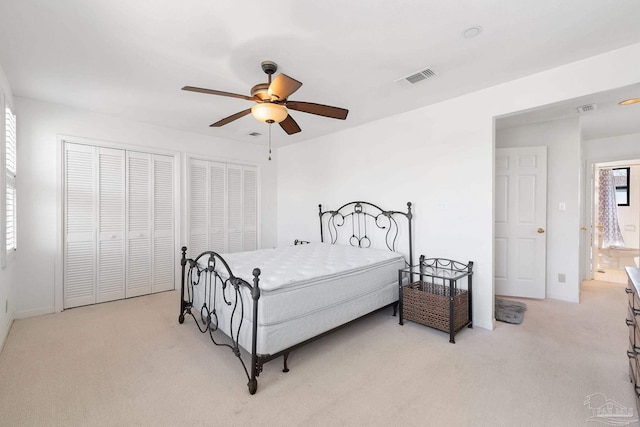 bedroom with light carpet, visible vents, two closets, and ceiling fan
