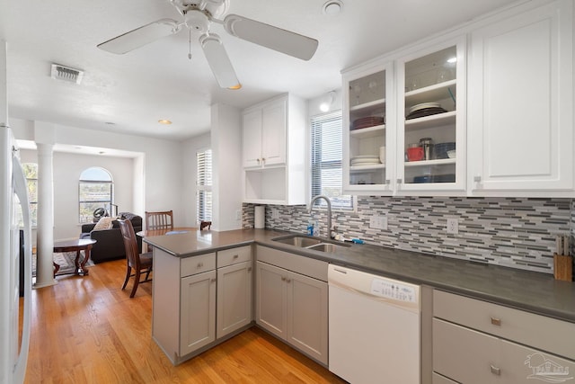 kitchen with visible vents, a peninsula, white appliances, dark countertops, and a sink