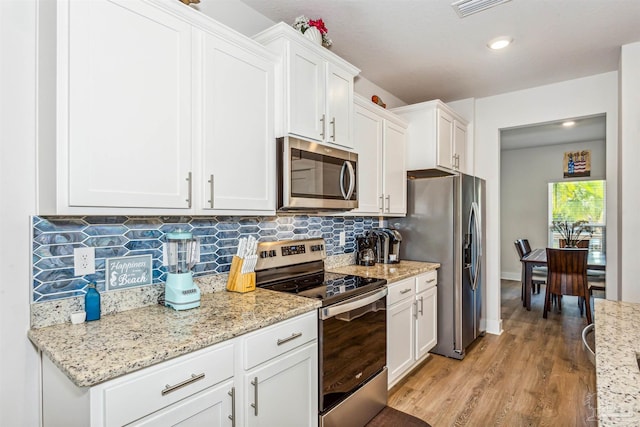 kitchen featuring light hardwood / wood-style floors, light stone countertops, backsplash, white cabinets, and appliances with stainless steel finishes