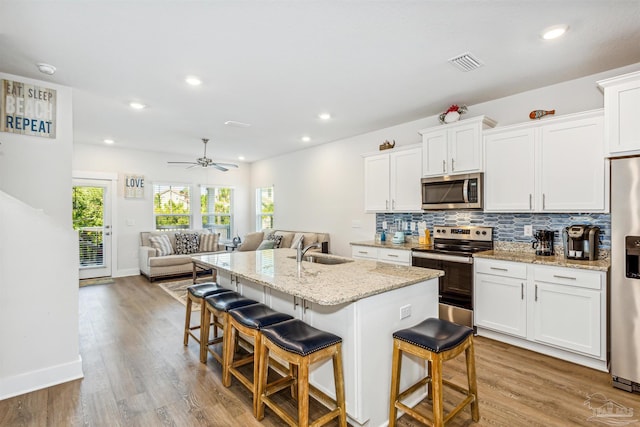 kitchen featuring light hardwood / wood-style floors, a kitchen island with sink, a breakfast bar, white cabinets, and appliances with stainless steel finishes