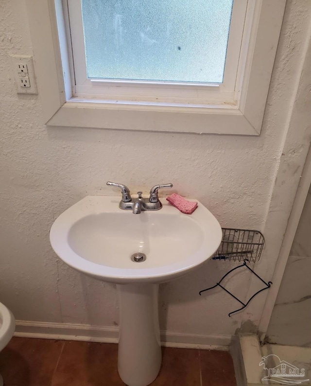 bathroom featuring baseboards, tile patterned flooring, and a textured wall